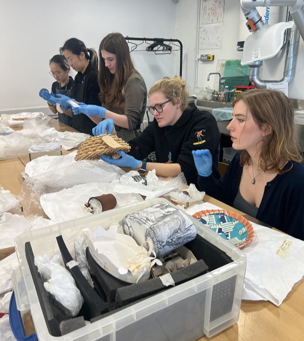 A group of students at a large table examining pieces from the Crafts Council's handling collection. 